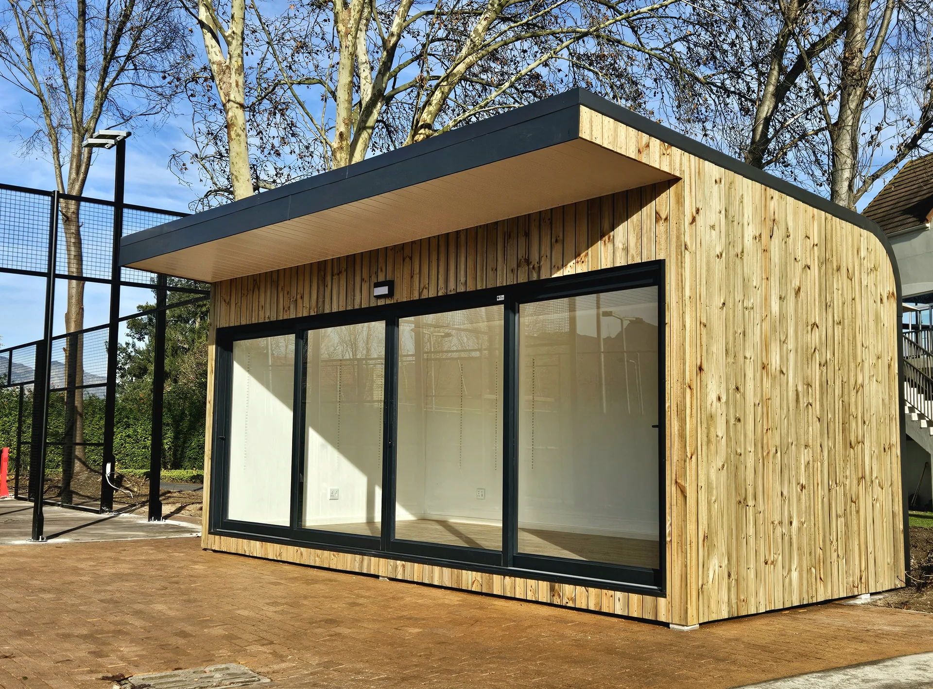 Timber-clad pro shop with an angled roof and sliding glass frontage, on a paved surround beside trees