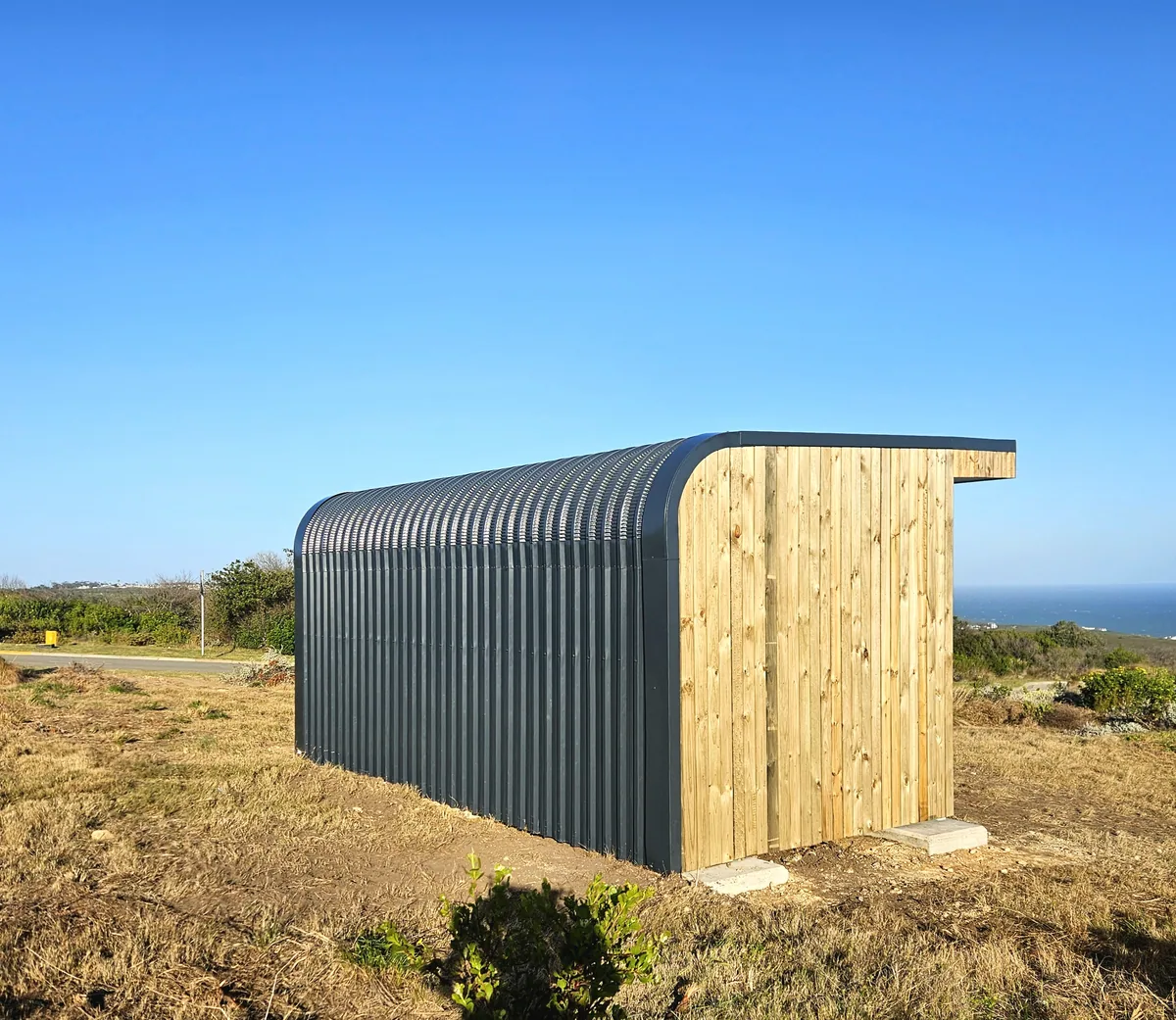 Rear of a pod clad in timber and curved corrugated steel, standing in coastal fynbos