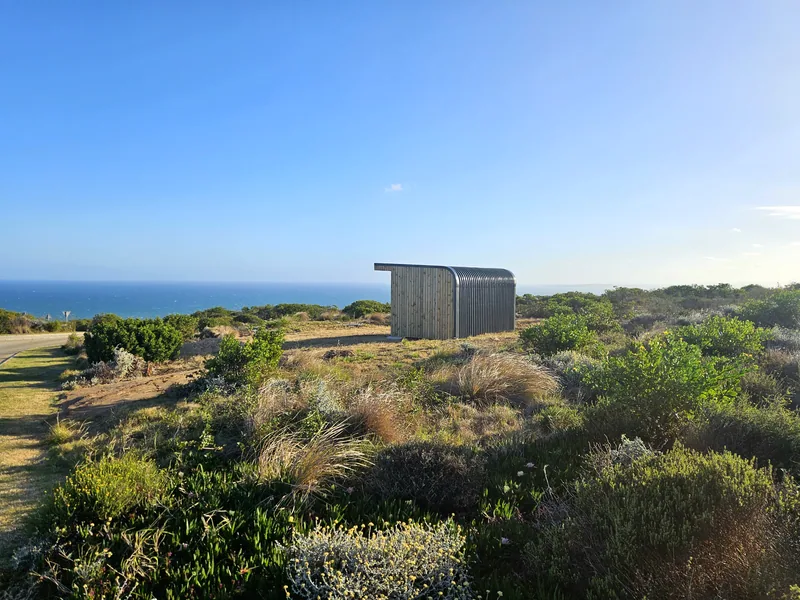 Distant view of a small pod set in coastal fynbos with the sea and horizon behind