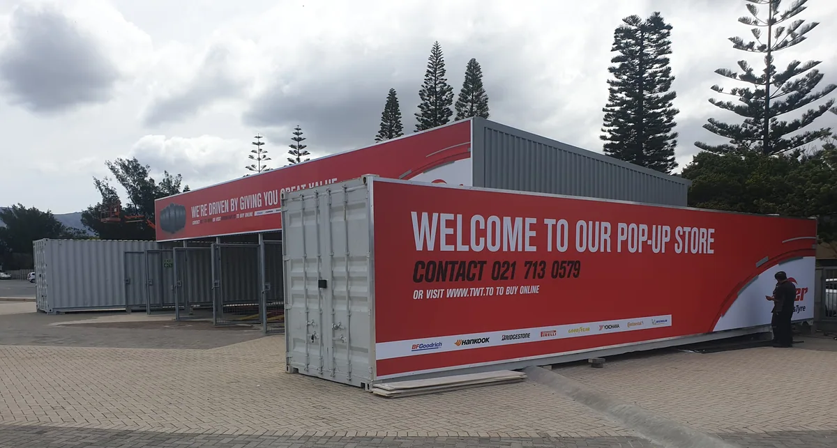 Container units forming a pop-up tyre store, with large red branded banners along the roofline