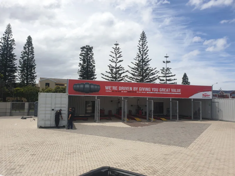 Pop-up container store under construction on a paved forecourt, with red branded signage above the openings
