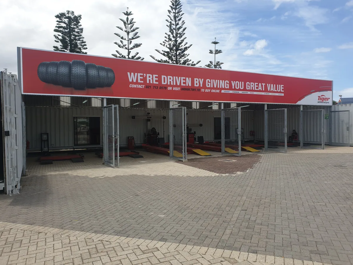 Front elevation of a container pop-up tyre store with a long red branded banner and open service bays