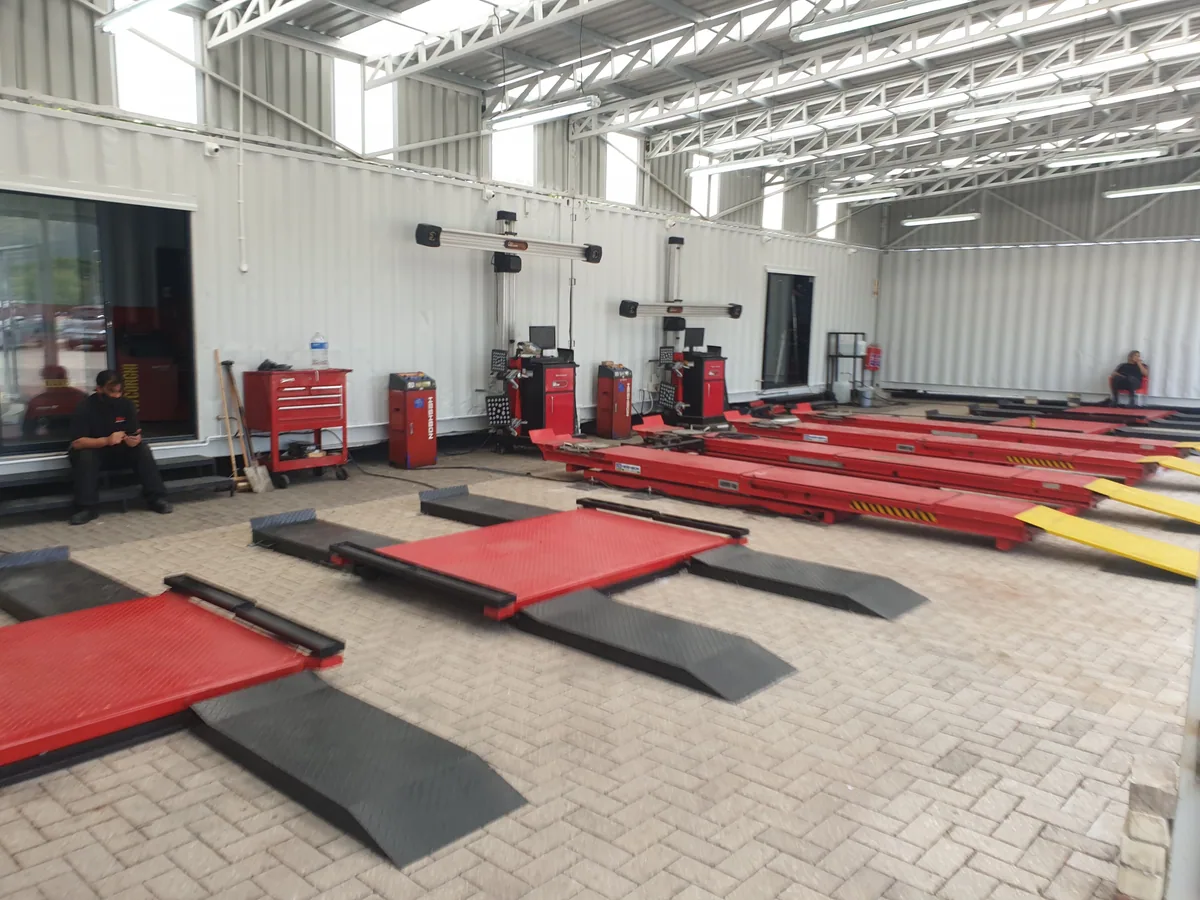 Interior of a container-built tyre fitment workshop with red wheel alignment ramps and equipment trolleys