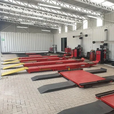 Wide view of a tyre fitment workshop interior with rows of red alignment ramps under a steel roof