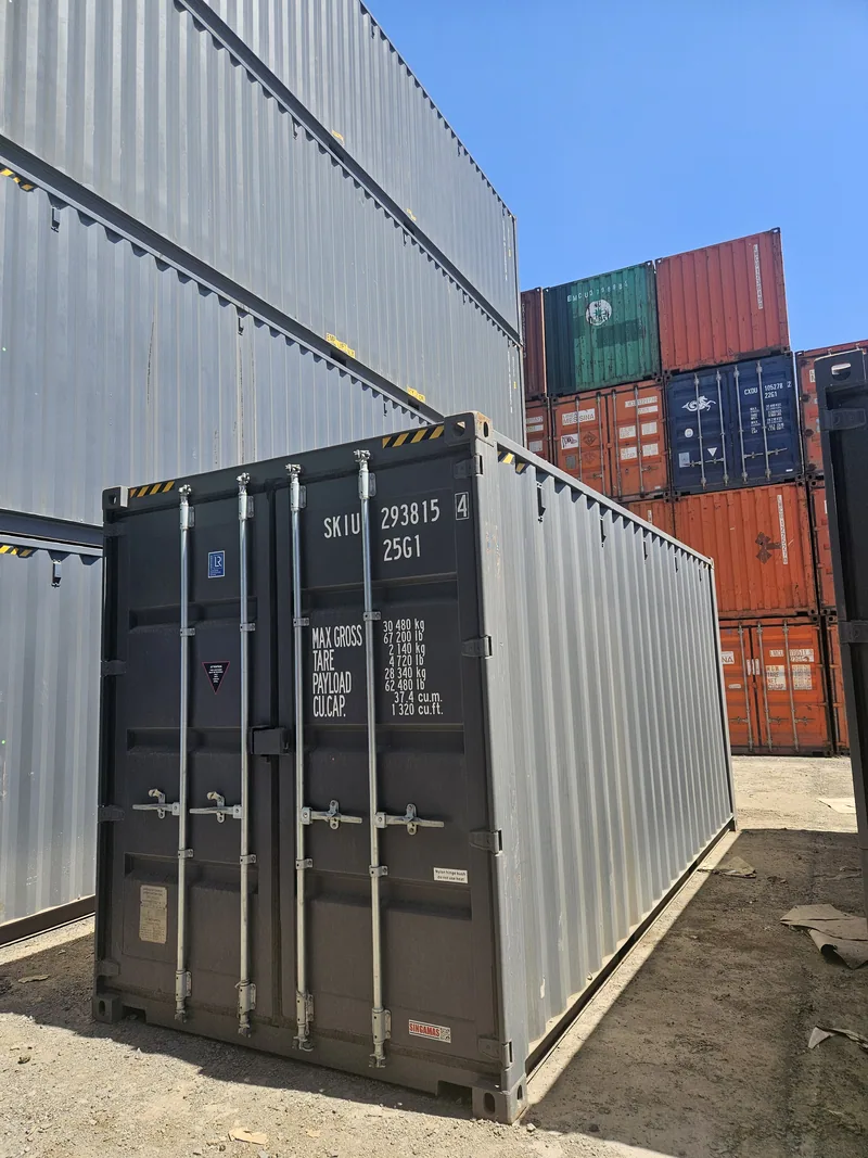 Grey shipping container in a stacking yard with other containers behind it and identification markings on the door