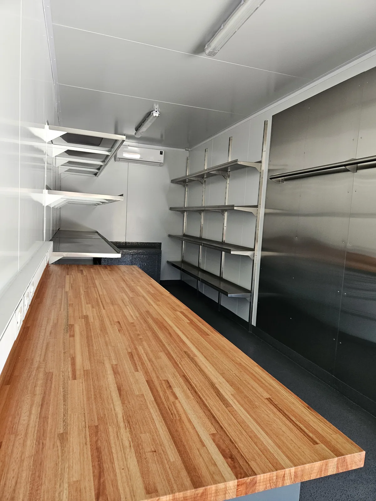 Container workshop interior with a butcher-block timber worktop and stainless steel shelving along the walls