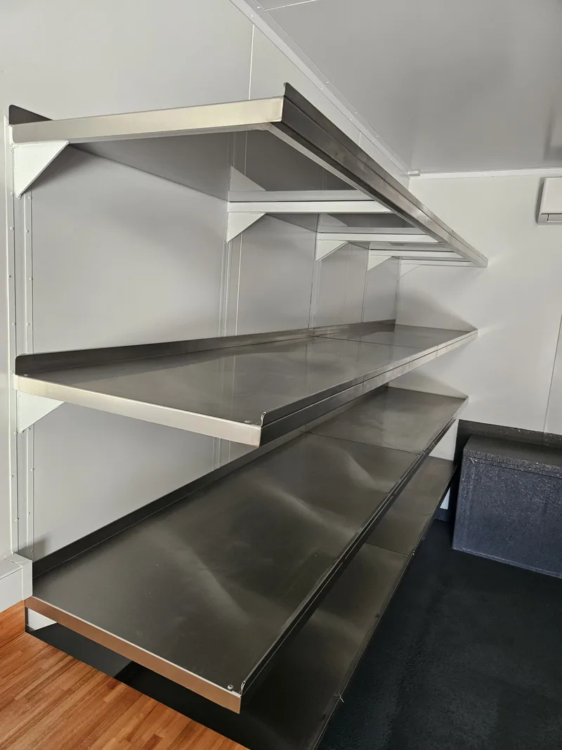 Close view of stainless steel shelving above a timber worktop inside a fitted container
