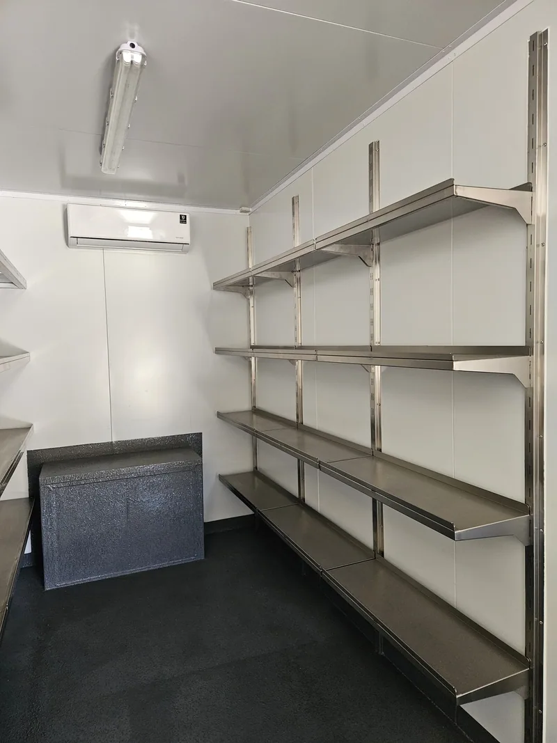 Stainless steel shelving racks fitted along the white-lined wall of a container workshop
