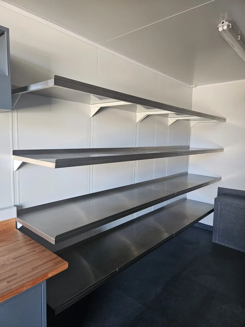 Stainless shelves and a stainless bench above a timber worktop in a container interior