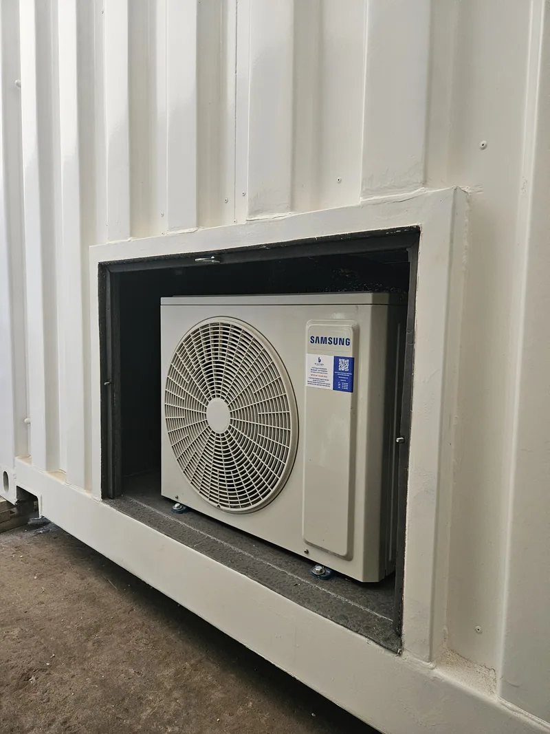 External air-conditioning unit mounted in a framed recess cut into a white container wall