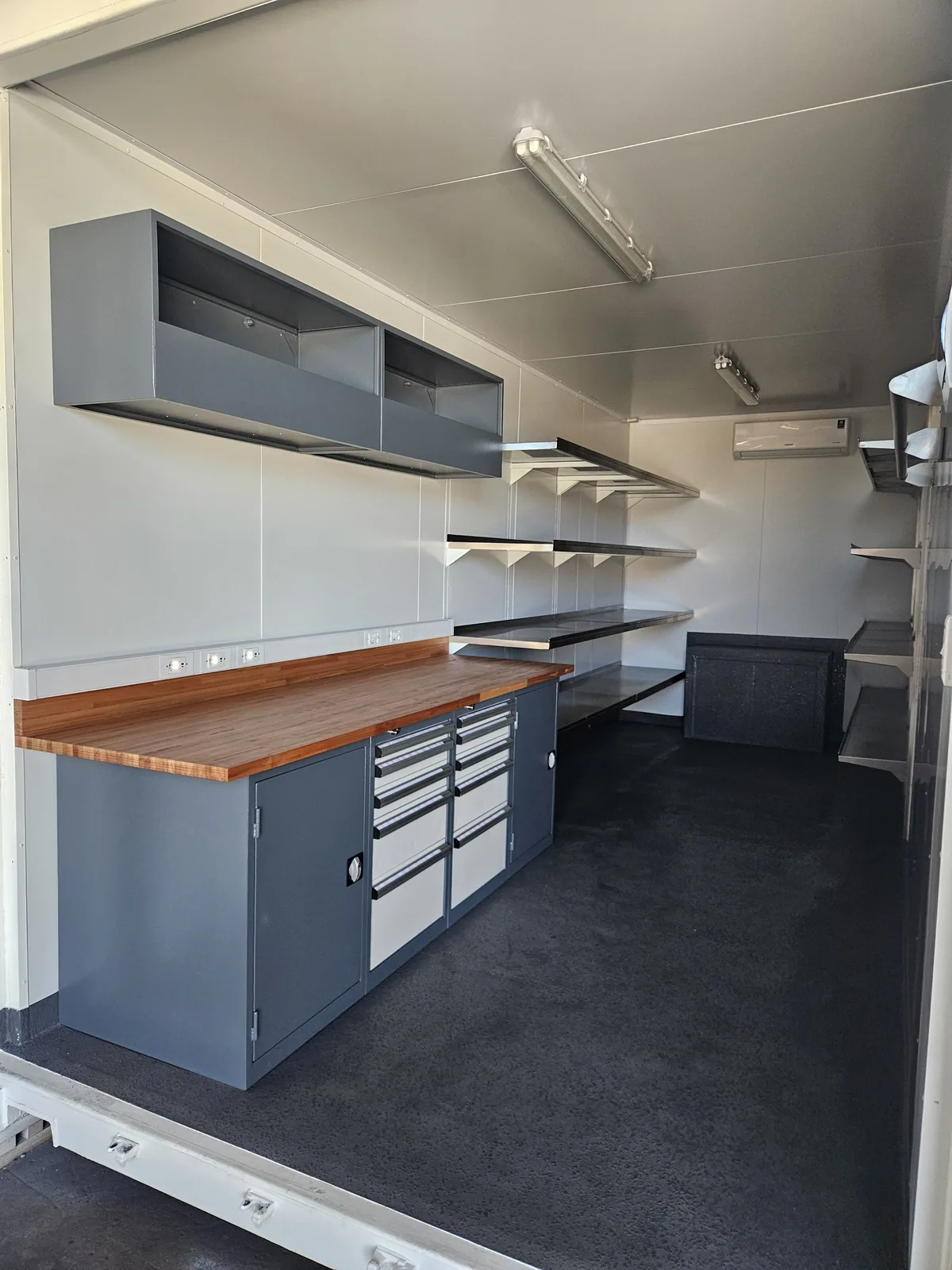 Fitted container workshop with a timber-topped tool bench, drawer unit and overhead cabinets
