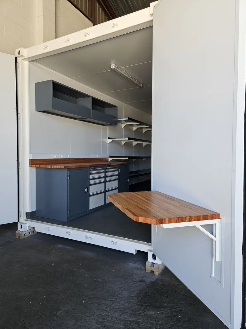 Fold-down timber bench and tool drawer unit inside a fitted container workshop